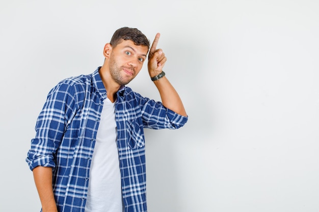 Young male pointing up finger in shirt and looking curious , front view.