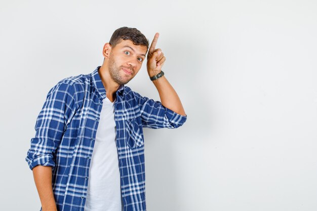 Young male pointing up finger in shirt and looking curious , front view.