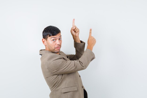 Young male pointing up in grayish brown jacket,black shirt and looking careful .