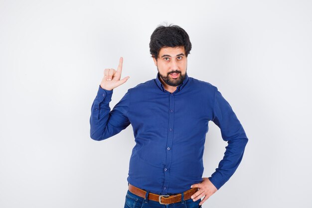 Young male pointing up in shirt, jeans and looking confident , front view.