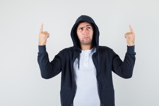 Young male pointing up in t-shirt, jacket and looking hesitant. front view.