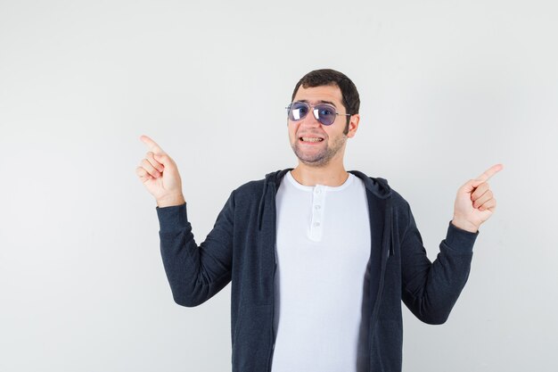 Young male pointing up in t-shirt, jacket and looking merry. front view.