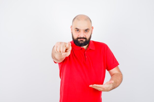 Young male posing like holding something while pointing at camera in red shirt , front view.
