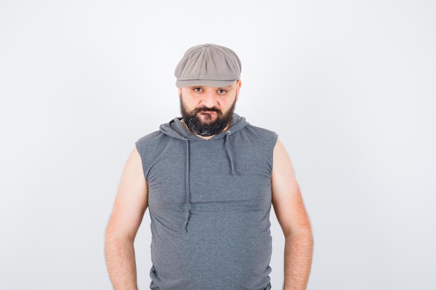 Young male posing while standing in sleeveless hoodie, cap and looking confident. front view.