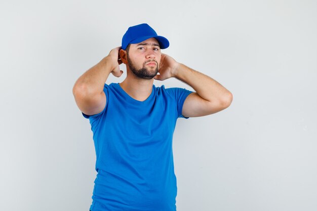 青いTシャツとキャップで頭の後ろの手でポーズをとって真剣に見える若い男性