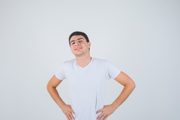 Young male posing with hands on waist in t-shirt and looking cheery , front view.
