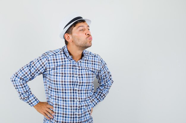 Young male pouting lips and holding hands on waist in checked shirt