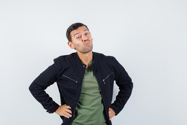 Young male pouting lips with hands on waist in t-shirt, jacket , front view.