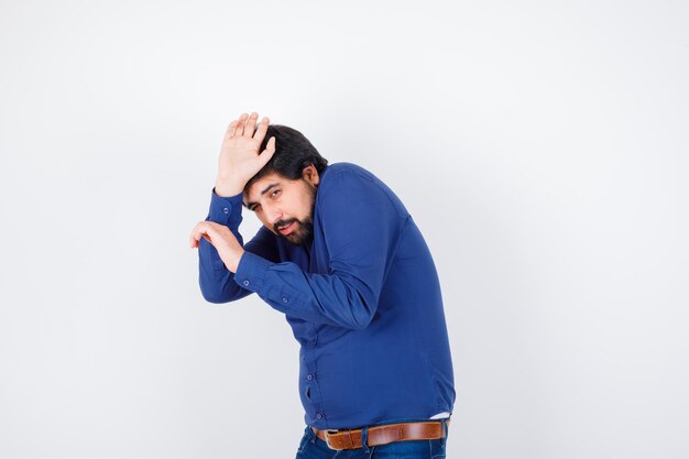 Young male pretending to defend himself in shirt, jeans and looking scared , front view.