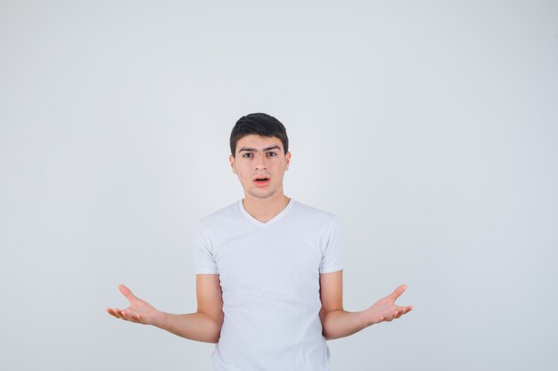 Young male pretending to show something in t-shirt and looking focused. front view.