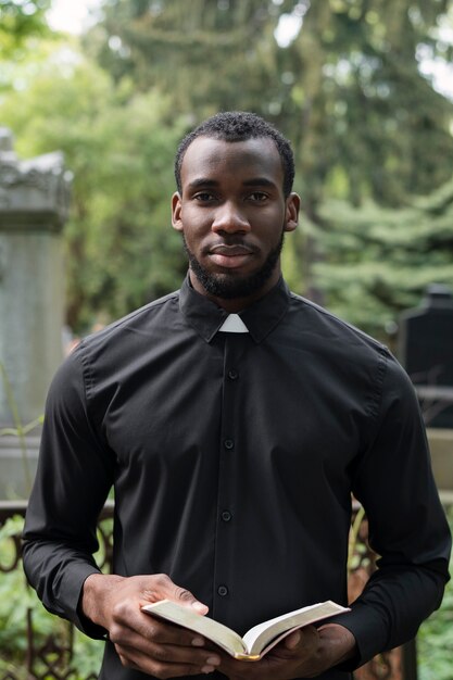 Молодой священник-мужчина держит библию на кладбище