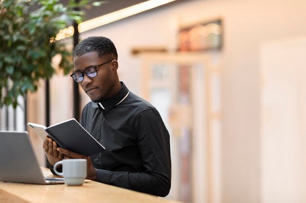 Молодой священник читает книгу в кафе