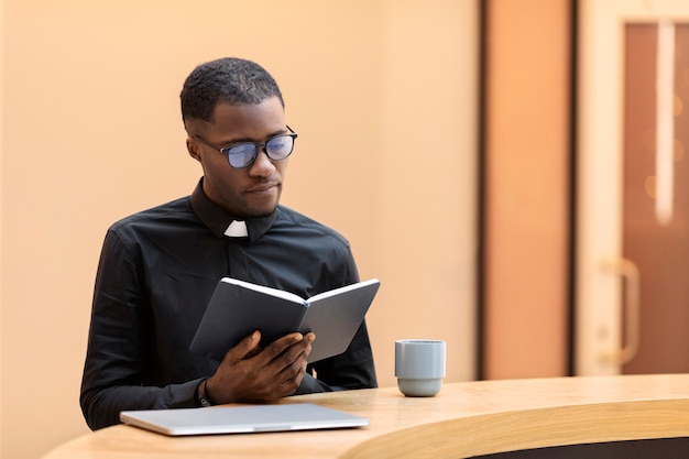 Young male priest reading a book at the cafe