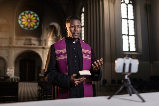 Young male priest streaming the sermon from church with smartphone