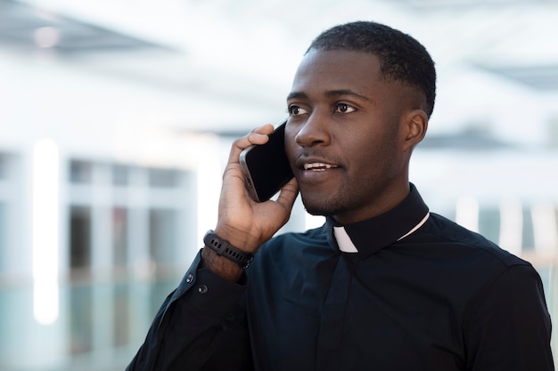 Young male priest talking on smartphone