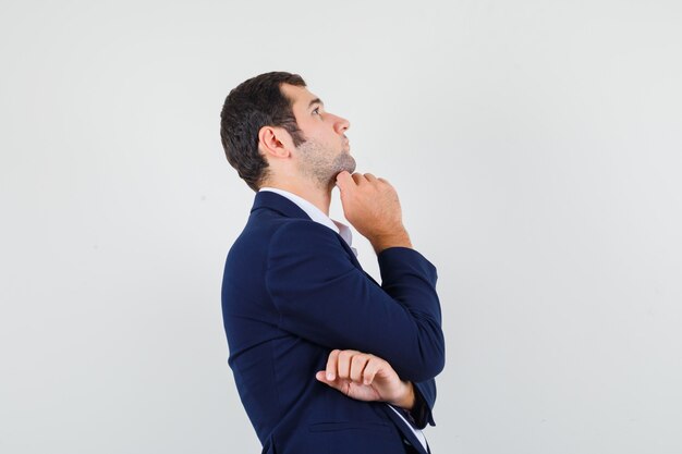 Young male propping chin on hand in shirt, jacket and looking pensive