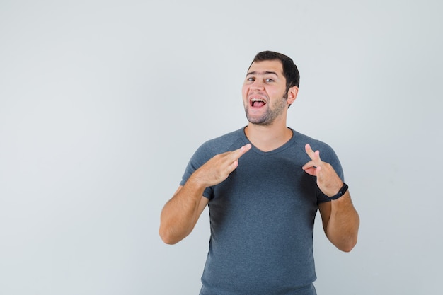 Young male pulling his t-shirt in grey t-shirt and looking proud 