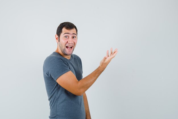 Young male raising hand in grey t-shirt and looking happy 