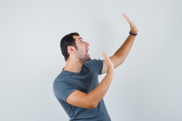 Young male raising hands to defend himself in grey t-shirt and looking agitated  