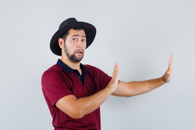 Foto gratuita giovane maschio alzando le mani per difendersi in t-shirt, cappello e guardando turbato. vista frontale.