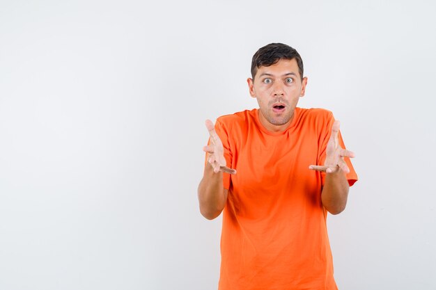 Young male raising hands in questioning gesture in orange t-shirt and looking perplexed