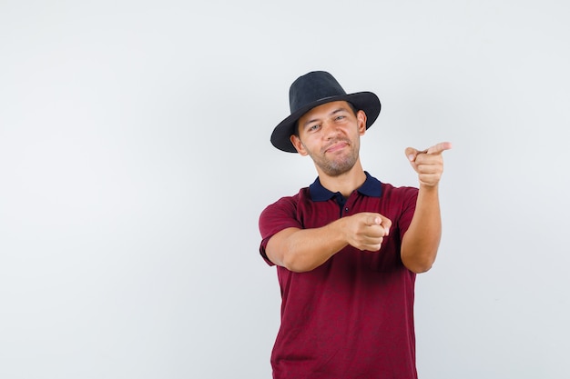 Young male in red shirt,black hat pointing forward and looking confident , front view.