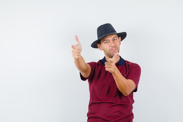 Young male in red shirt,black hat posing on camera and looking relaxed , front view.