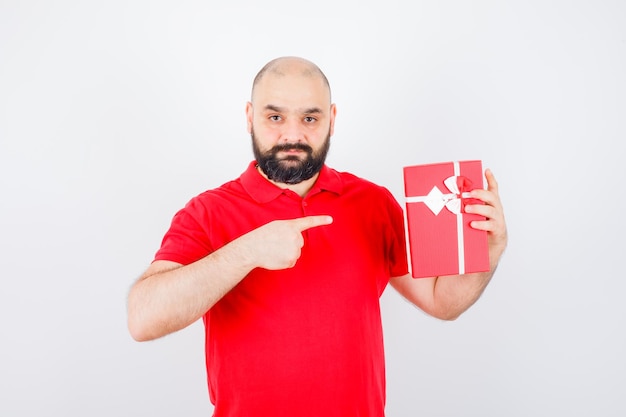 Young male in red shirt pointing at present box , front view.