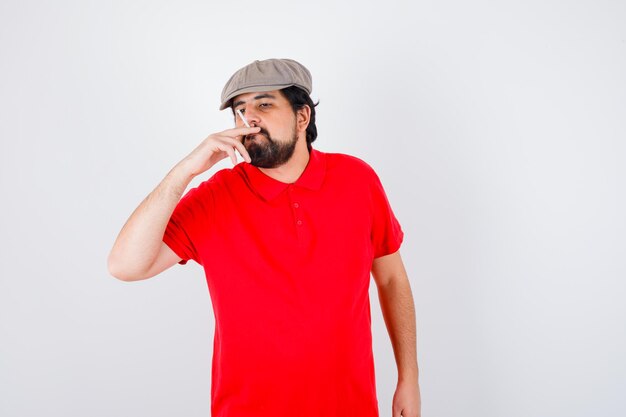 Young male in red t-shirt,cap smoking , front view.