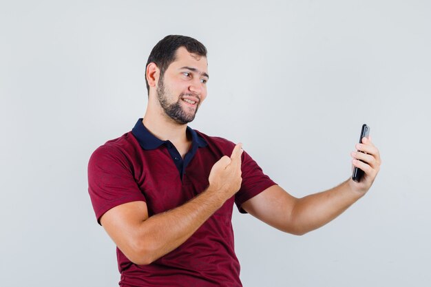 写真を撮って陽気に見ながらポーズをとる赤いTシャツの若い男性、正面図。