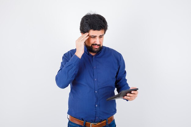 Young male in royal blue shirt calculating and looking troubled , front view.