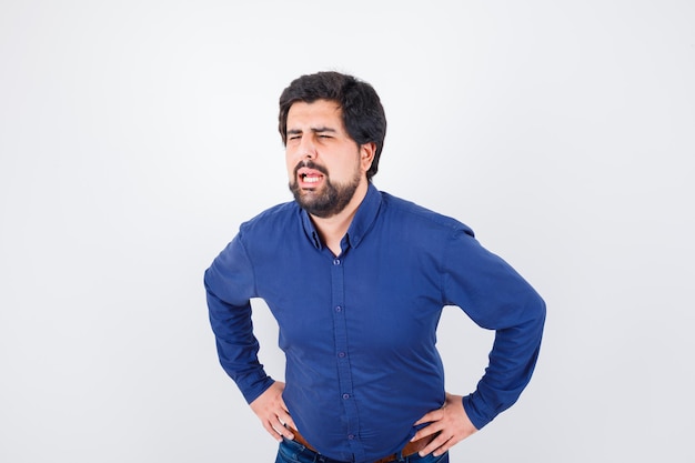 Young male in royal blue shirt calling someone with loud voice while standing with hands on waist , front view.