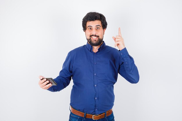 Young male in royal blue shirt holding phone while looking up , front view.