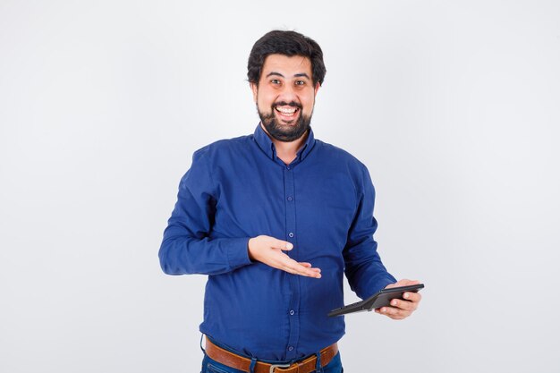 Young male in royal blue shirt showing calculator while laughing , front view.