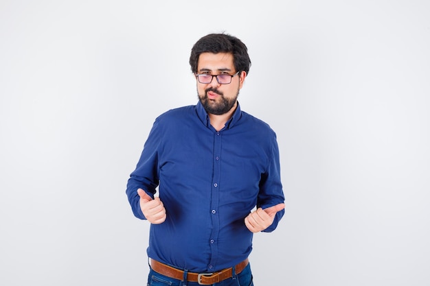 Young male in royal blue shirt, showing thumb up,pouting lips and looking joyful , front view.