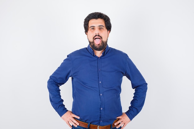 Young male in royal blue shirt sticking tongue out and looking weird , front view.