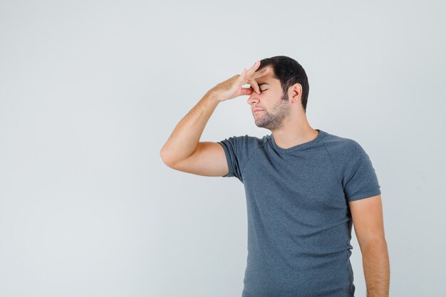 Young male rubbing eyes and nose in grey t-shirt and looking tired. front view.