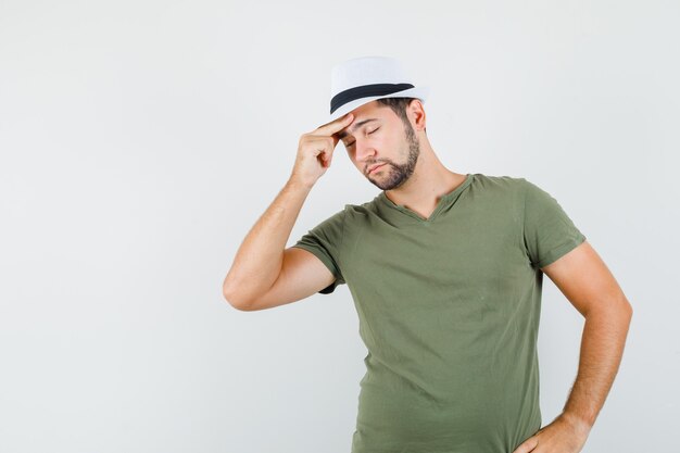 Young male rubbing temples in green t-shirt and hat and looking fatigued