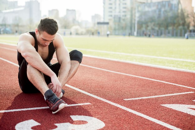 Young male runner sitting on race track looking at his shoes