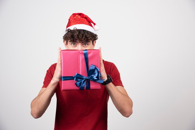 선물 상자 뒤에 숨어 산타 모자에 젊은 남성.