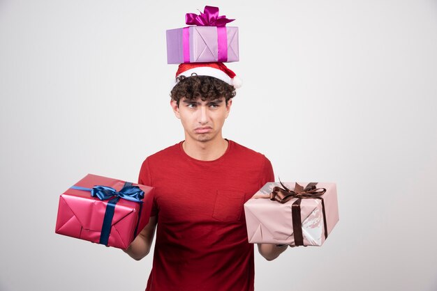 Young male in Santa hat holding gifts with bored expression.