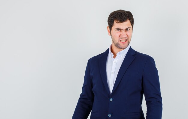 Young male scowling with clenched teeth in suit and looking gloomy , front view.