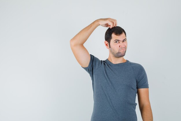 若い男性が灰色のTシャツで頭を掻き、躊躇しているように見える