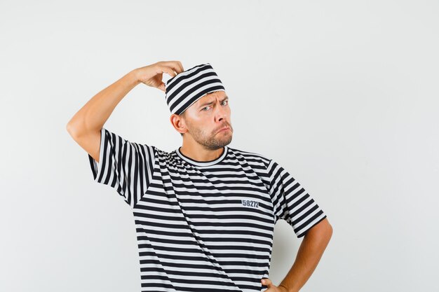 Young male scratching head in striped t-shirt hat and looking sullen  