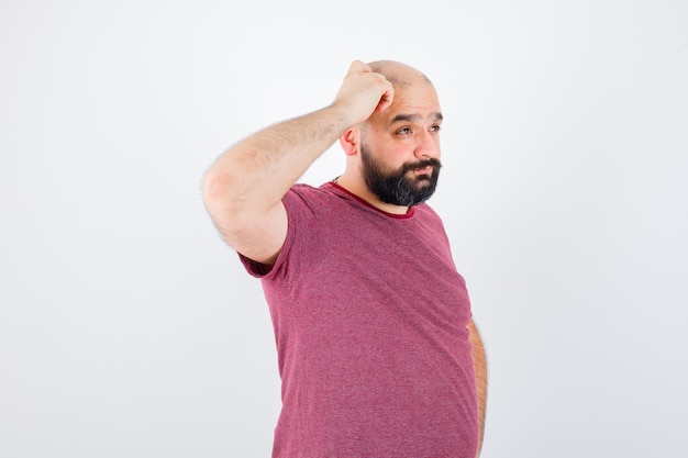 Young male scratching his head in pink t-shirt .