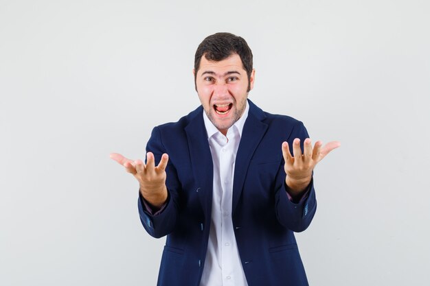 Young male screaming while stretching hands in questioning manner in shirt