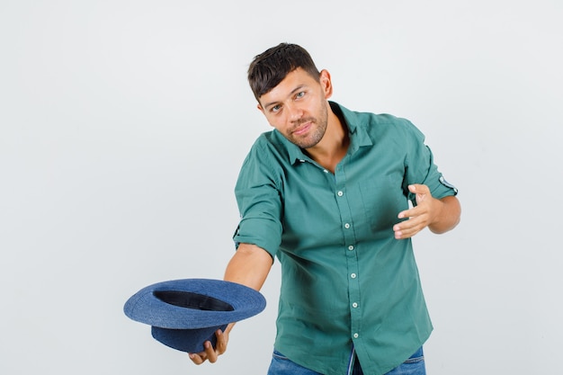 Foto gratuita giovane maschio in camicia inchinandosi e togliendosi il cappello e guardando allegro