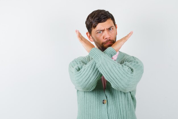 Young male in shirt, cardigan showing refusal gesture and looking serious , front view.