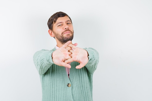 Free photo young male in shirt, cardigan stretching hands for strength and mobility and looking relaxed , front view.