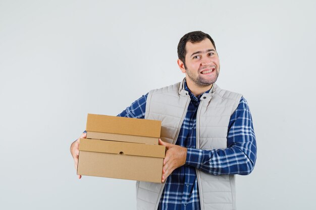 Young male in shirt,jacket carrying boxes and looking satisfied , front view.